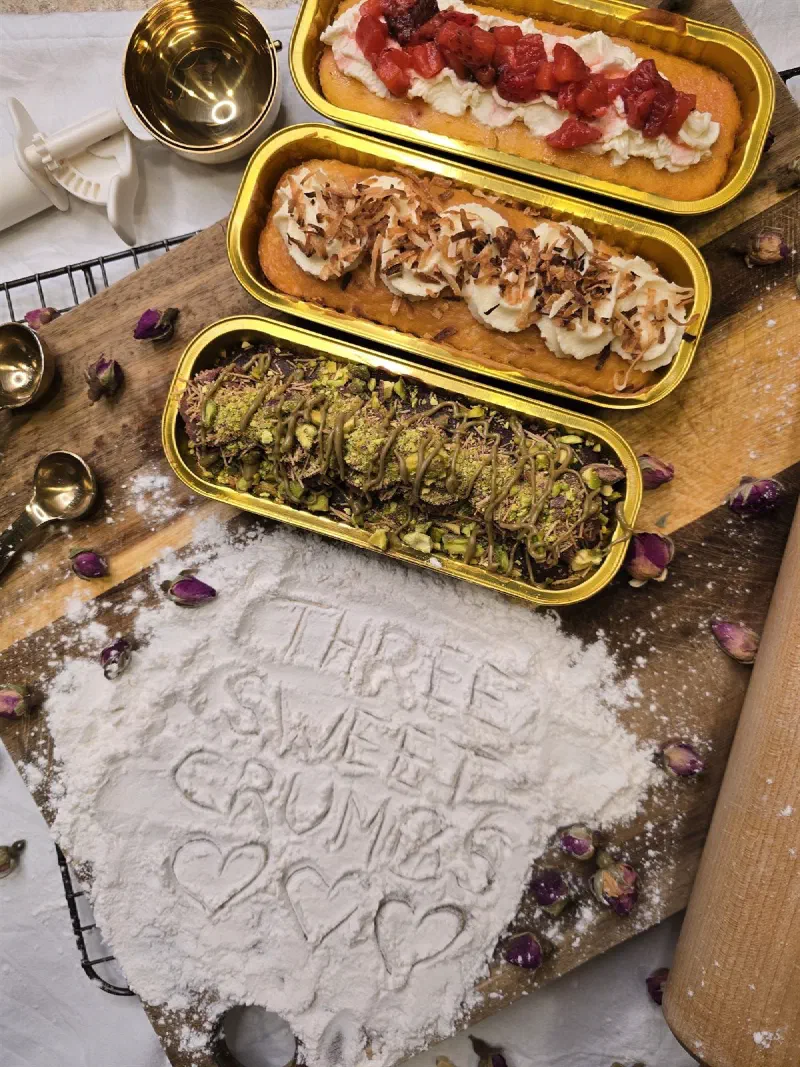 Three tin cakes on a floured board with "Three Sweet Crumbs" written in the flour