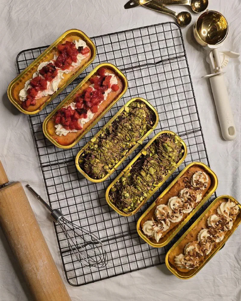 Six tin cakes on a cooling rack next to gold measuring spoons, a whisk and a rolling pin